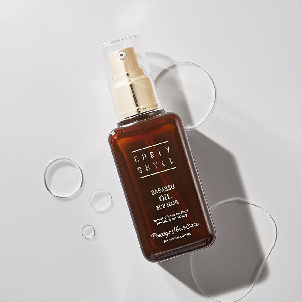 Flacone in vetro marrone con vaporizzatore dorato. Scritta: CURLY SHYLL, BABASSU OIL FOR HAIR, Prestige Clinic. Bolle d'acqua.
