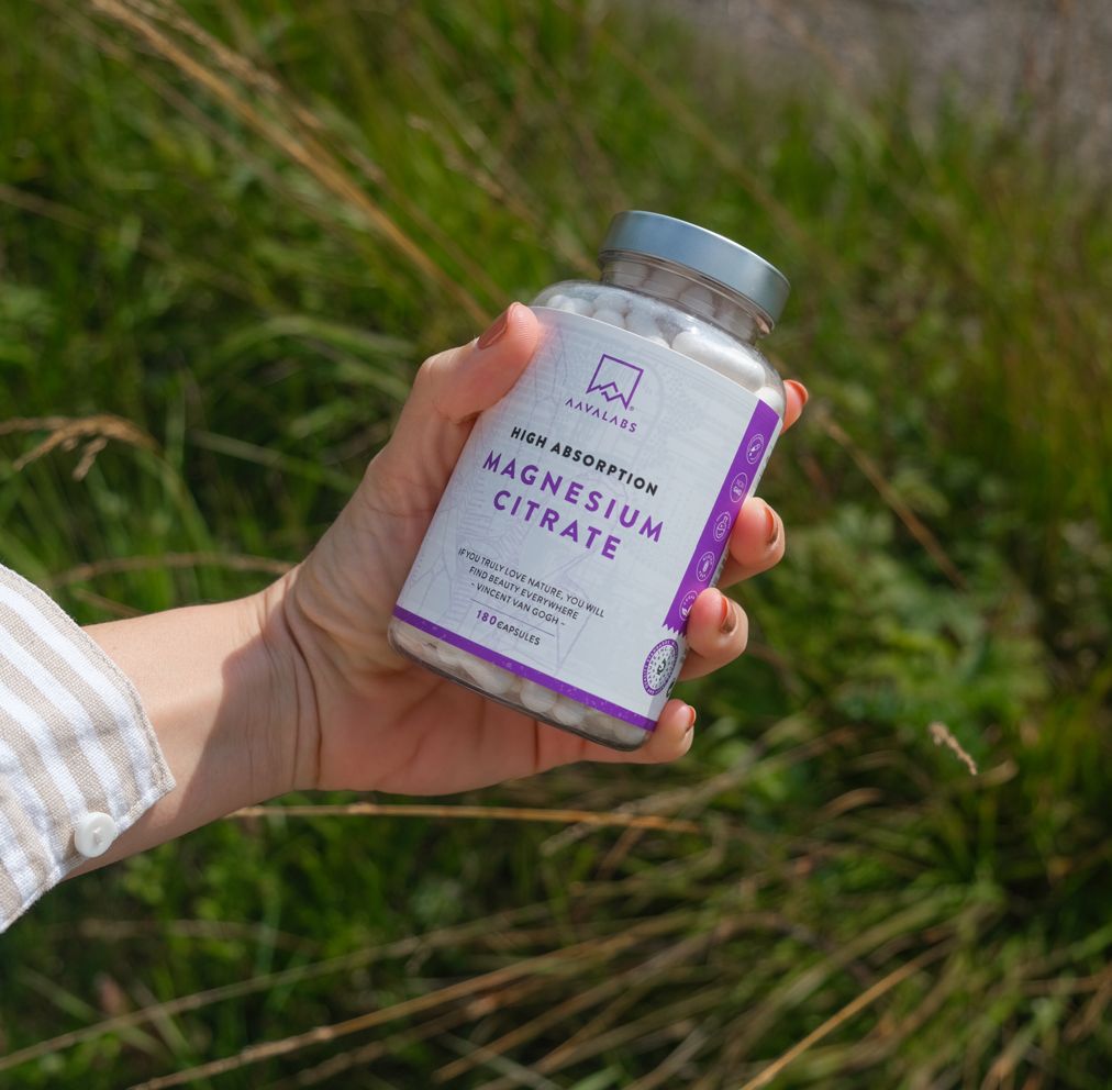 Una mano tiene in mano un flacone di capsule di citrato di magnesio. Scritta: High Absorption Magnesium Citrate. 180 capsule.