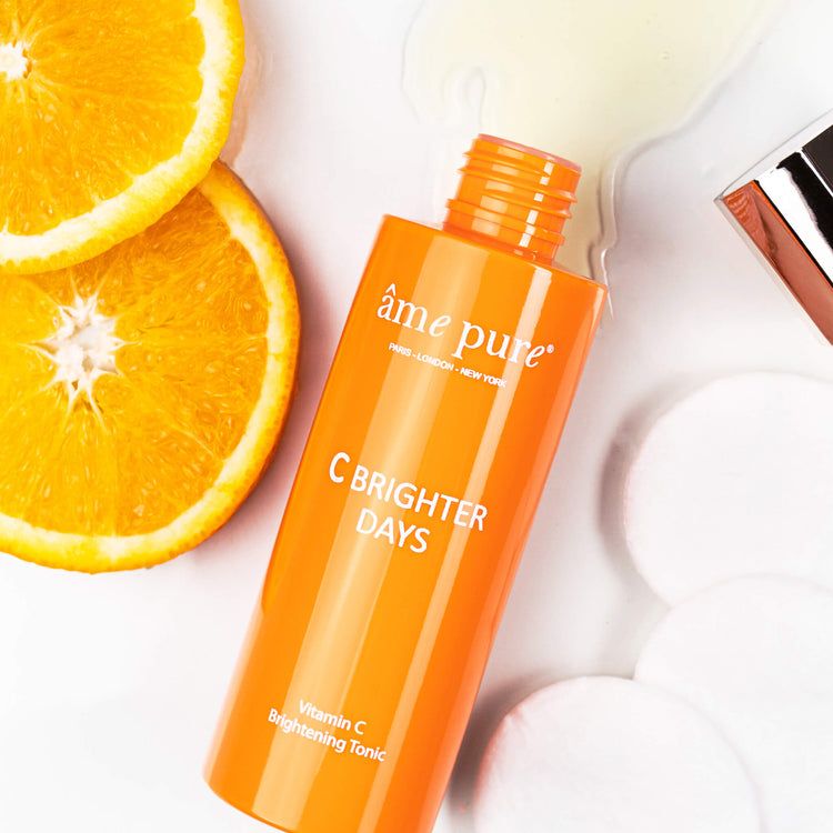 Flacone arancione con scritta âme pure C BRIGHTER DAYS. Accanto fette d'arancia e dischetti di cotone.