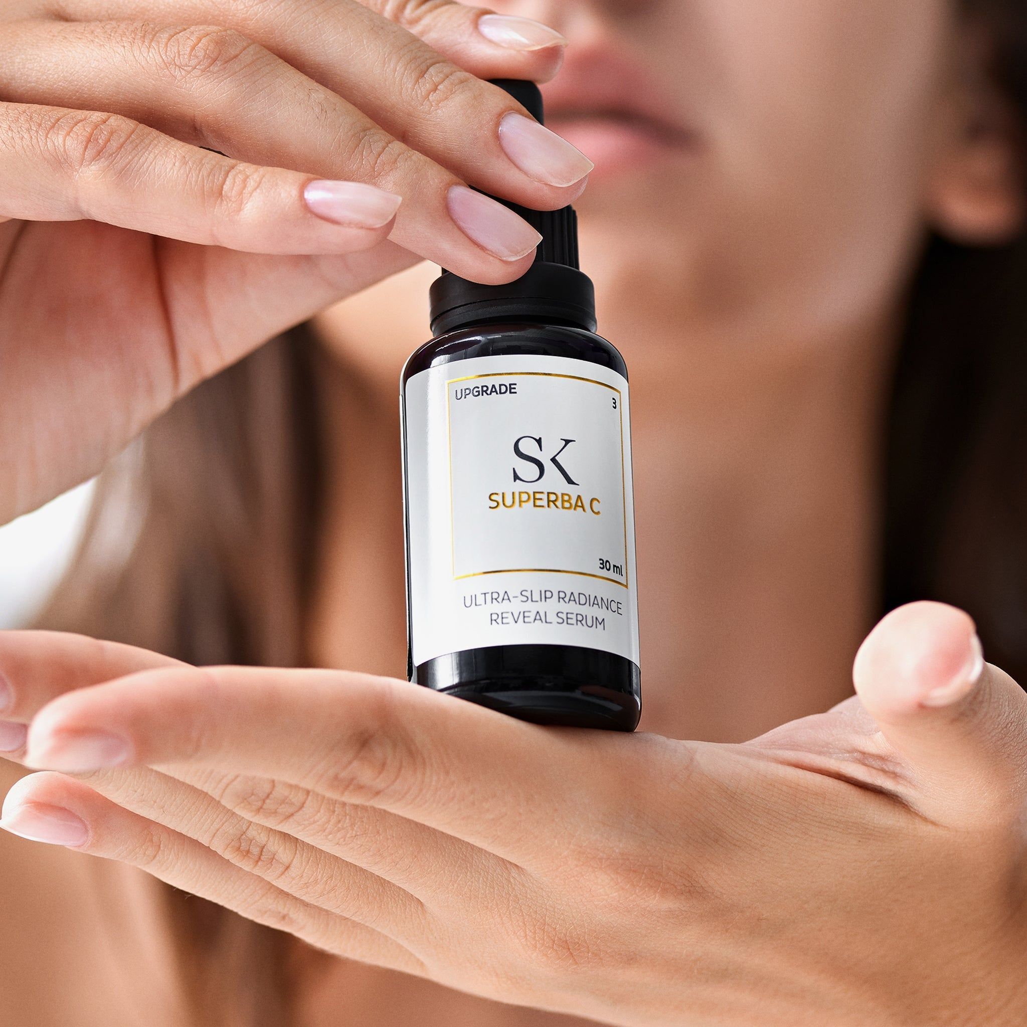 Mani che tengono un flacone nero con pipetta. L'etichetta indica "SK SUPERBA C" e "ULTRA-SLIP RADIANCE REVEAL SERUM".