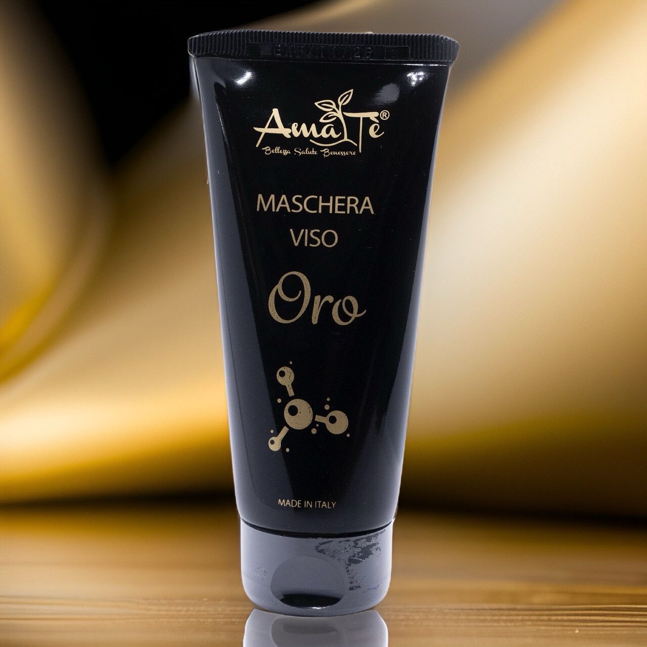 Tubo nero con testo dorato. Scritta: Amatè, Maschera Viso, Oro. Prodotto in Italia. Su sfondo dorato.