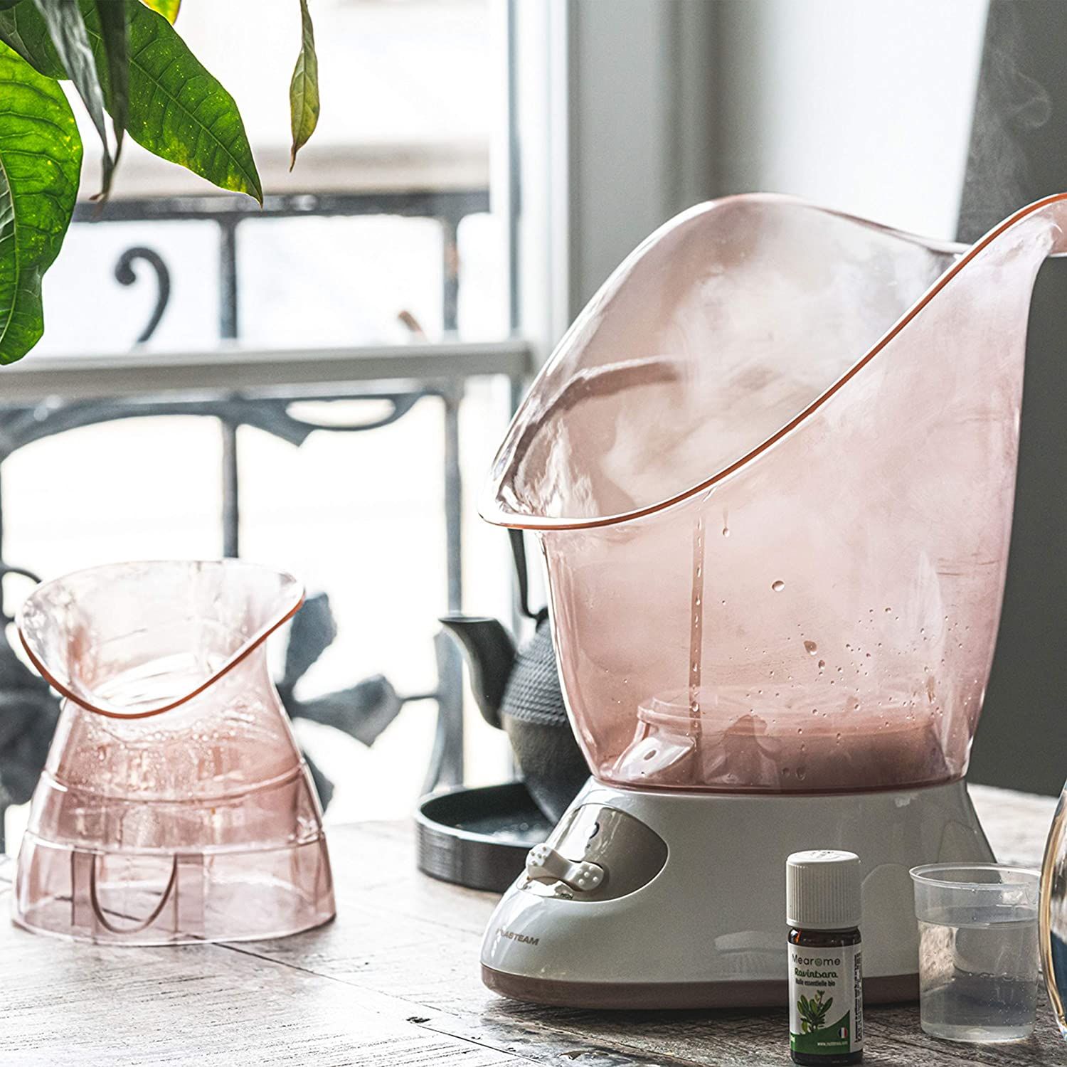 Sauna facciale bianca e rosa. Olio essenziale e misurino accanto.