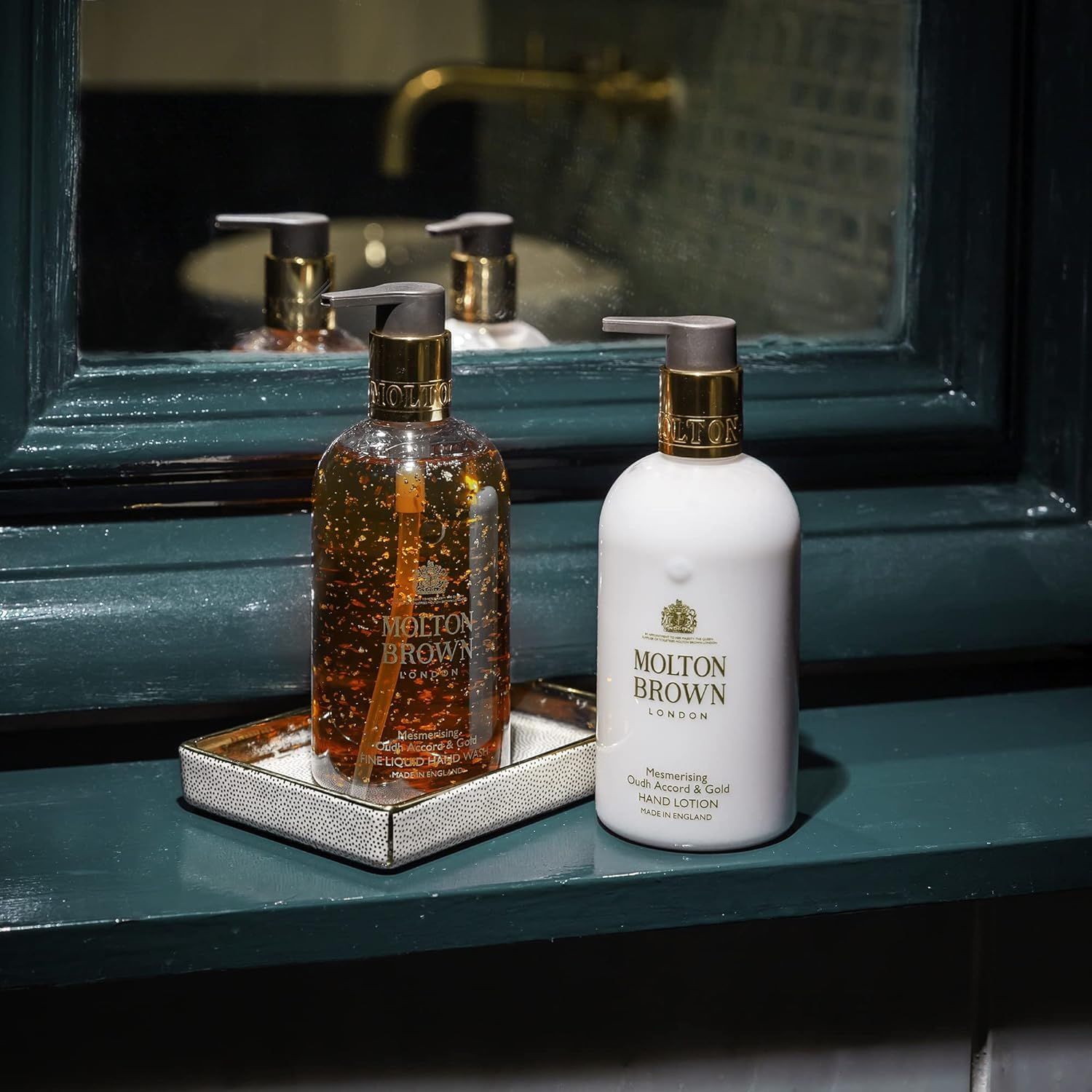 Due flaconi di lozione per le mani su un vassoio. Riflesso. Logo Molton Brown visibile.