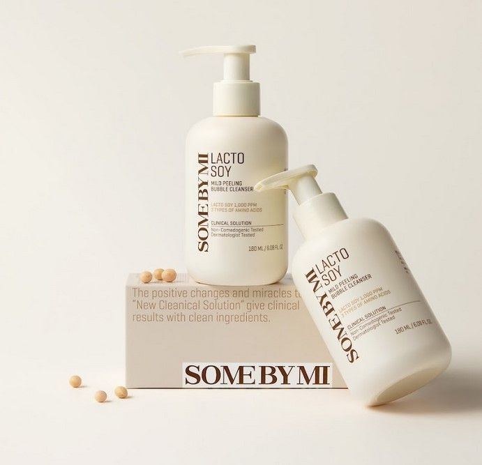 Due flaconi bianchi con pompa. Scritta: SOMEBYMI Lacto Soy Mild Bubble Cleanser. Confezione con testo e semi di soia.