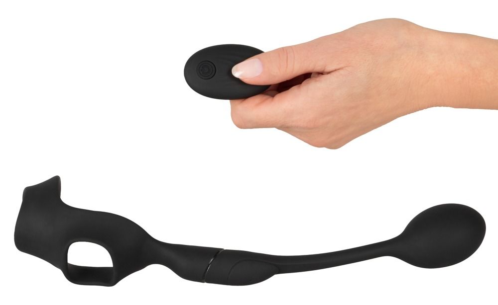 Mano che tiene un telecomando. Anello fallico nero con anello scrotale e plug anale accanto.
