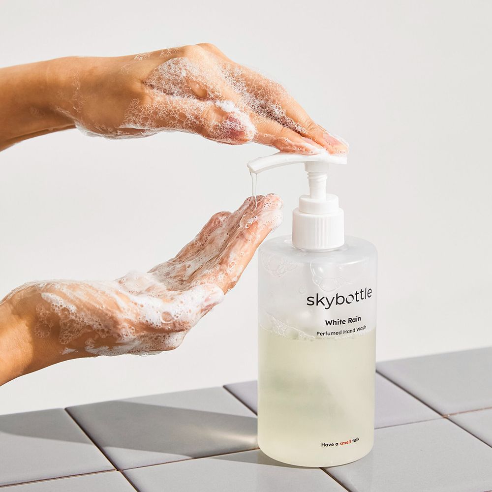 Mani che si lavano con il sapone per le mani SKYBOTTLE White Rain. Flacone trasparente con dosatore, schiuma sulle mani.