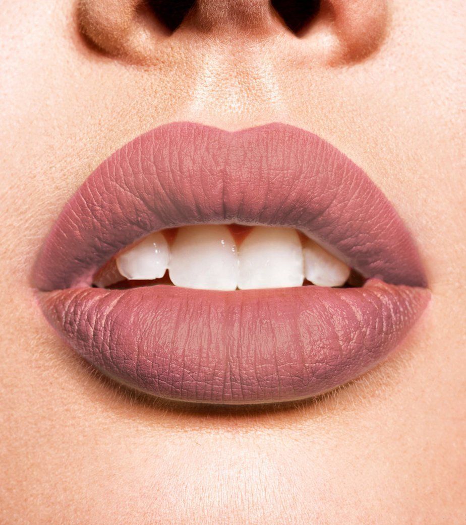 Primo piano di labbra con rossetto opaco color malva e denti bianchi.
