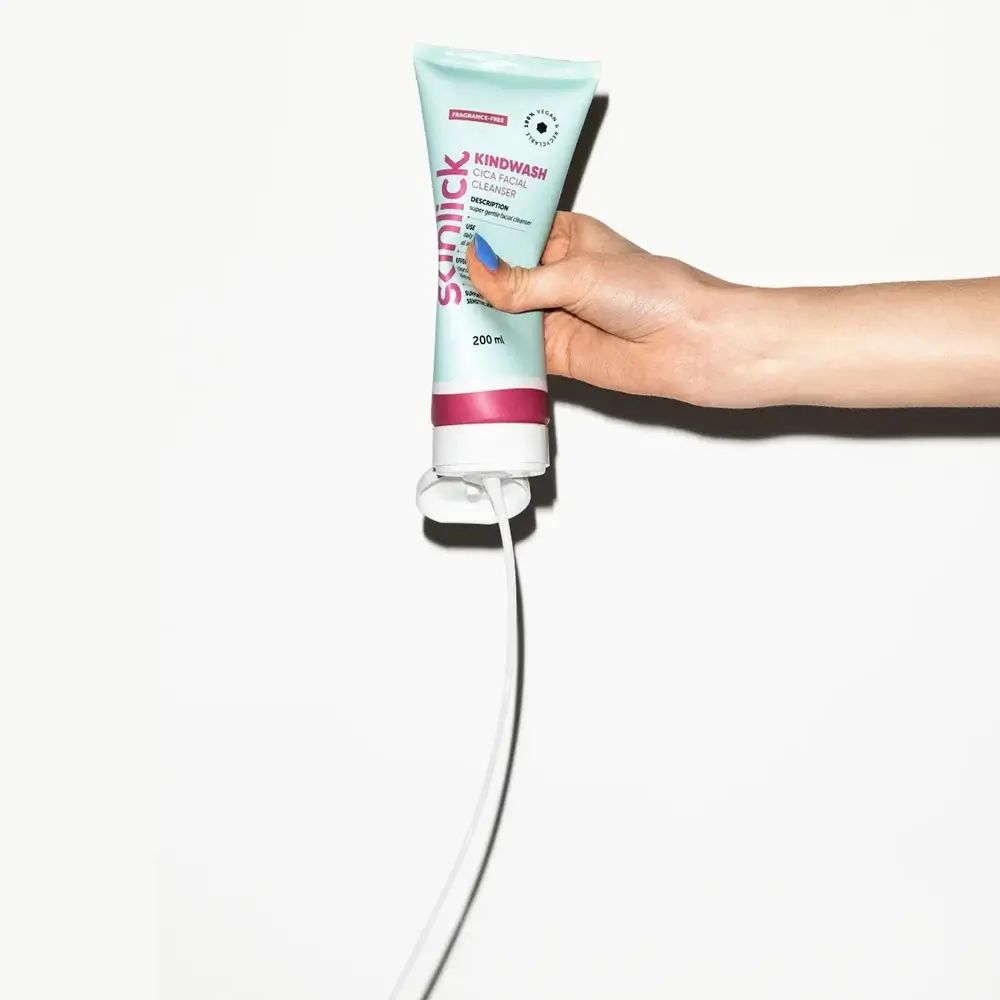 Tubo verde chiaro con striscia rosa. Testo: Kindwash, Cica Facial Cleanser. Prodotto tenuto in mano. Sfondo bianco.