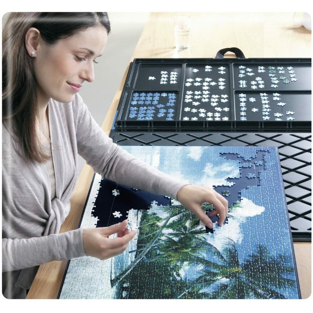 Donna che fa un puzzle su un tavolo. Contenitore nero per puzzle con pezzi. Pezzi posizionati su un tappetino.