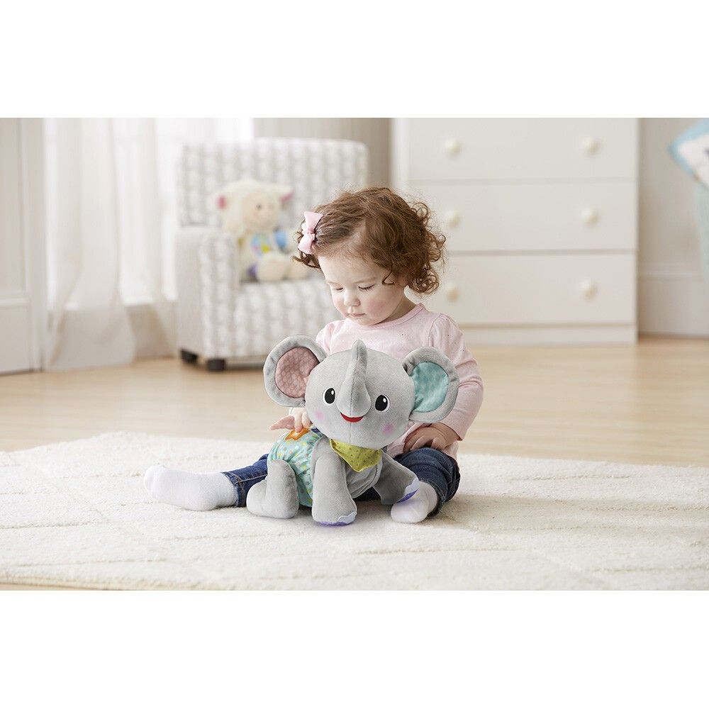 Bambino piccolo seduto che tiene un elefante grigio. Elefante con orecchie colorate e pannolino.