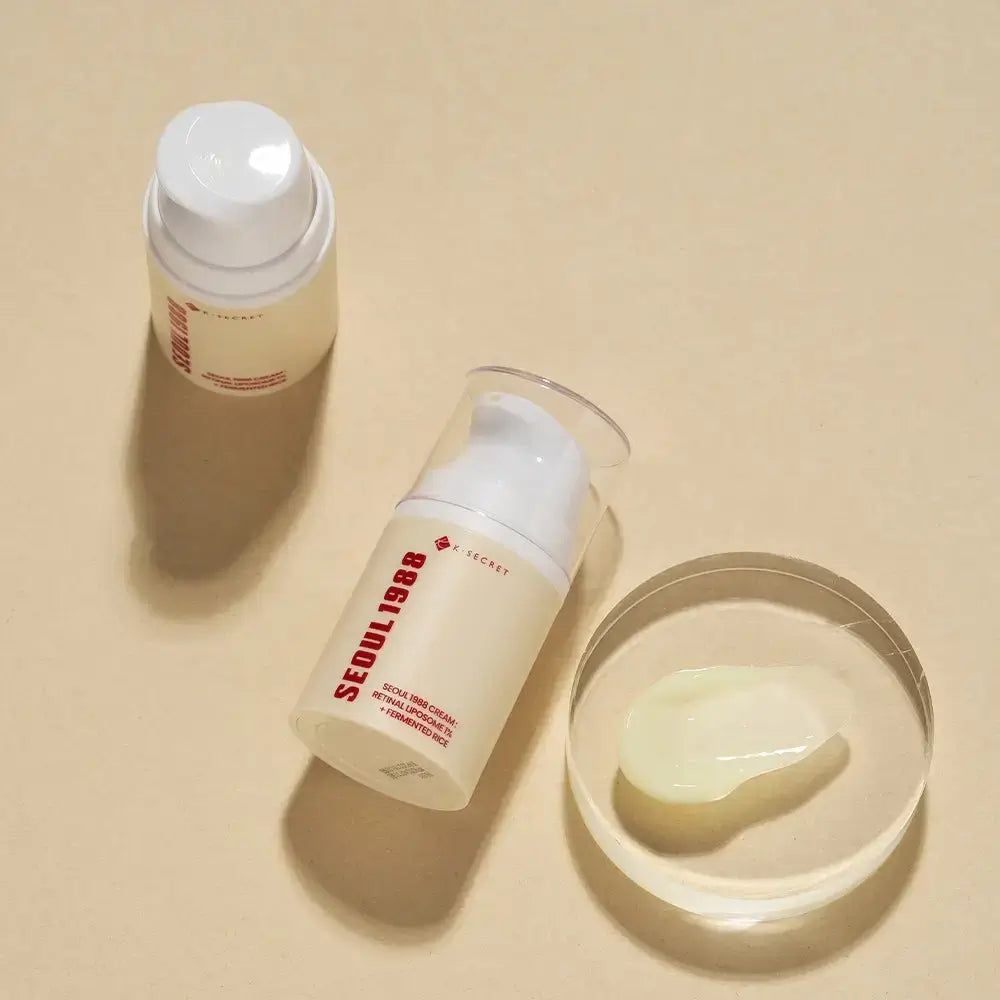 Due contenitori di crema e crema su una superficie trasparente. Scritta: SEOUL 1988, K-SECRET. Testo: RETINAL LIPOSOME 1% + FERMENTED RICE.