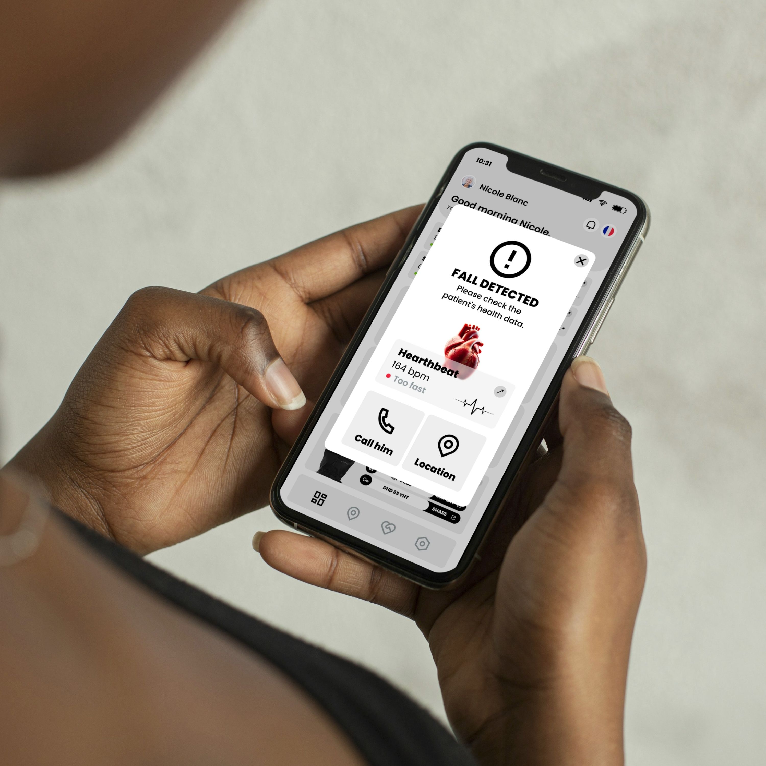 Persona che tiene in mano uno smartphone con interfaccia utente. Messaggio: "FALL DETECTED". Frequenza cardiaca: 164 bpm. Opzioni: Chiama, Posizione.