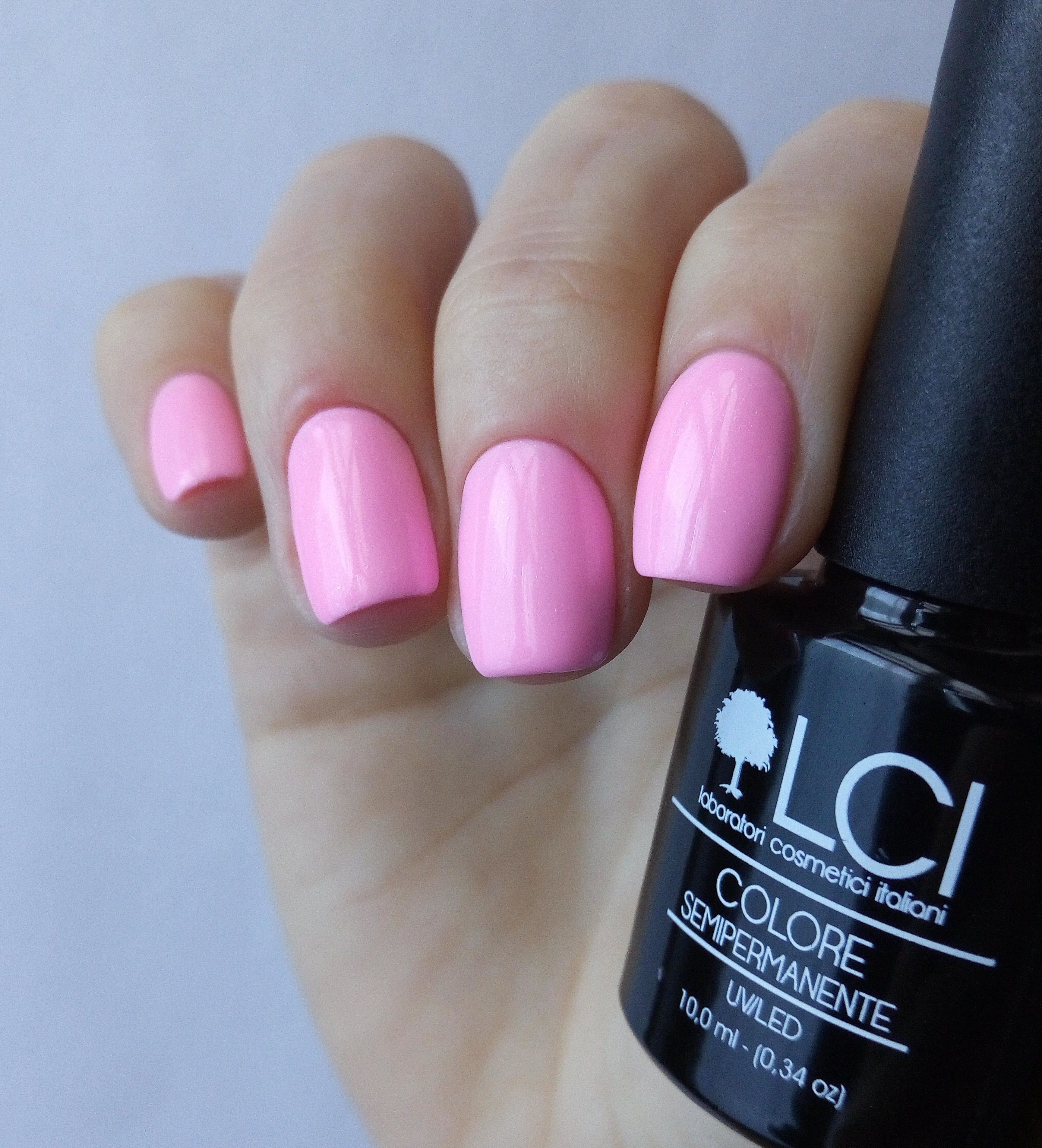 Mano con unghie rosa smaltate e flacone smalto. Scritta: LCI, Colore Semipermanente, UVLED.