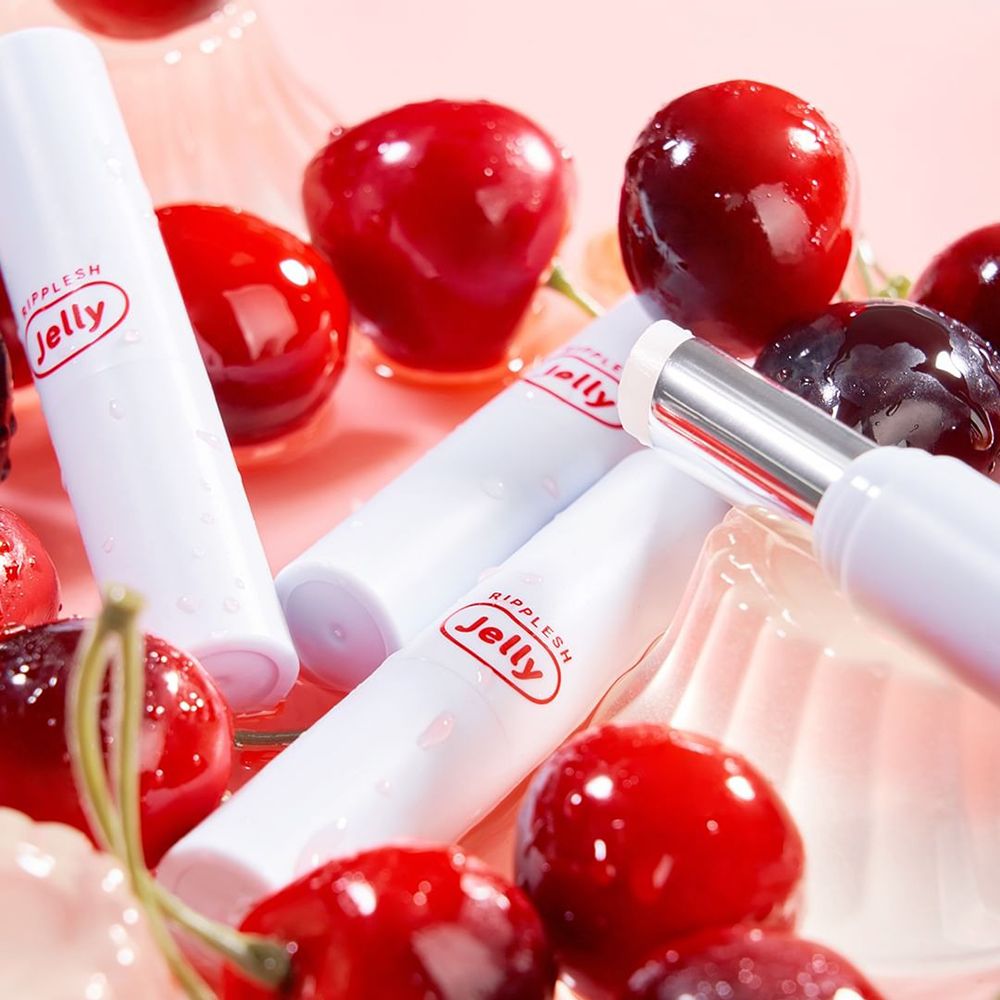 Stick di balsamo labbra bianchi con logo Jelly rosso, circondati da ciliegie. Alcuni stick sono umidi.