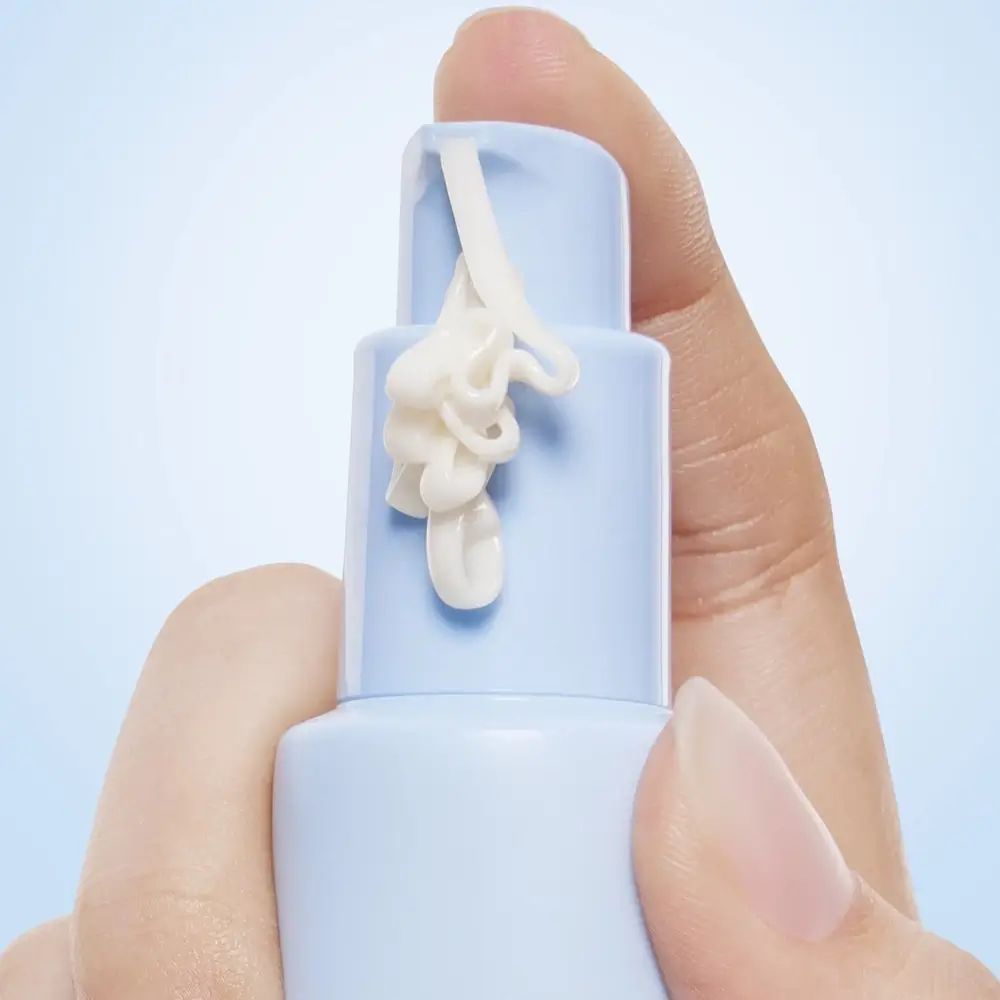 Crema chiara da flacone blu. Mano che tiene il flacone e preme per far uscire la crema.