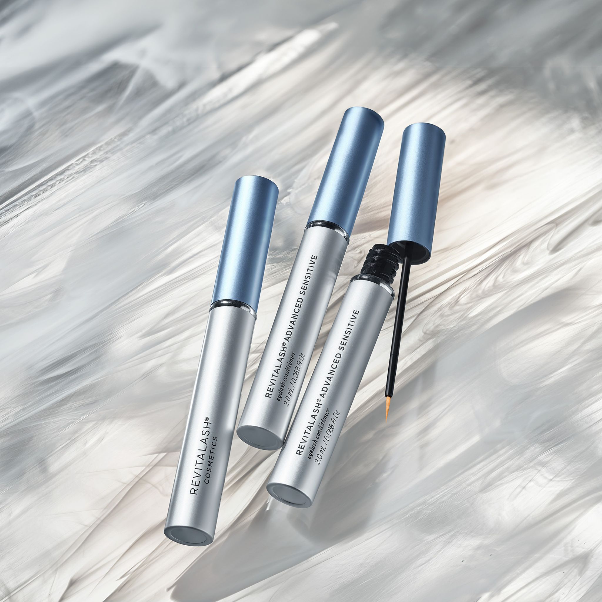 Tre flaconi RevitaLash® Advanced Sensitive, uno con applicatore aperto, su sfondo bianco.
