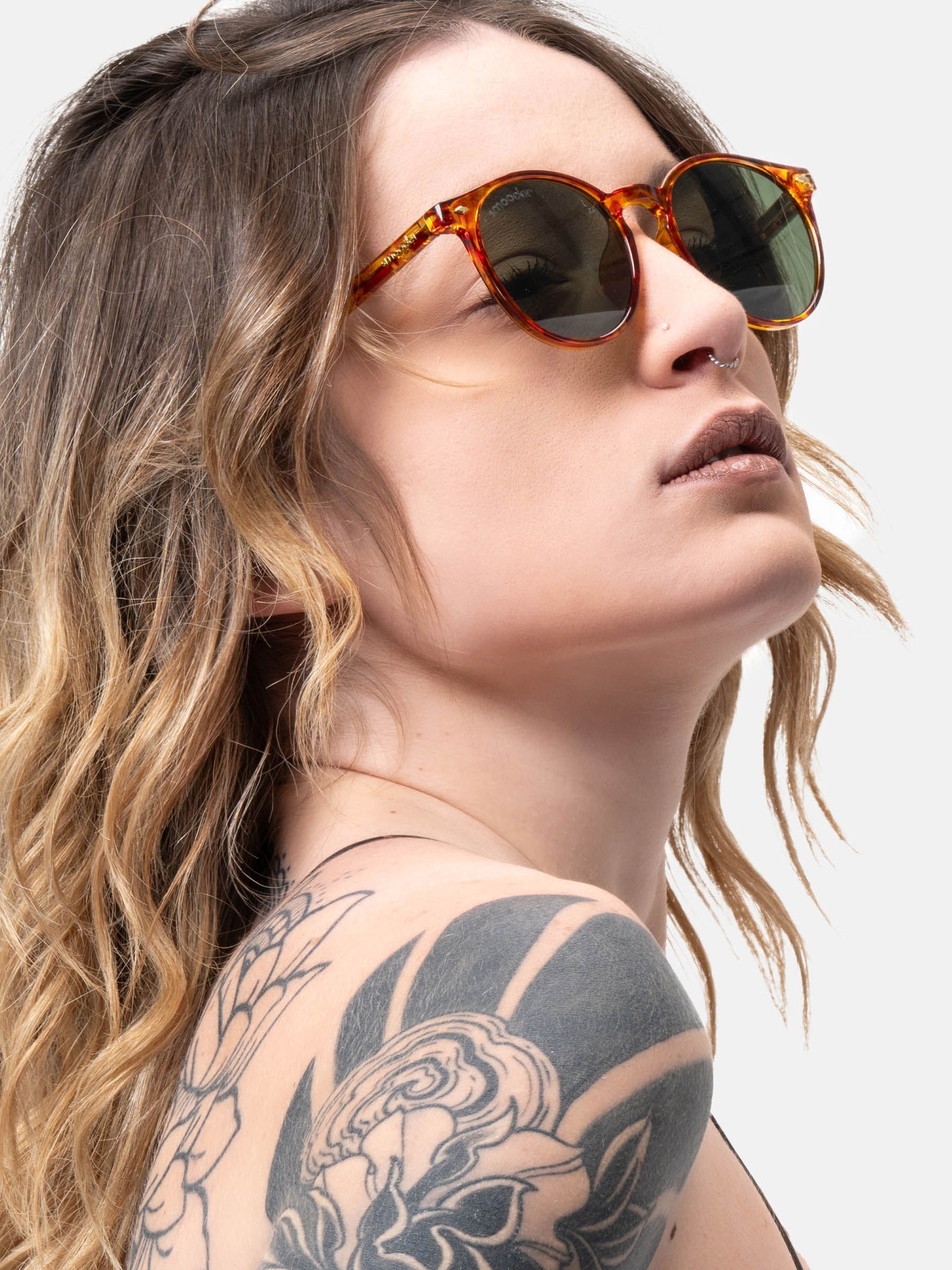 Persona con occhiali da sole marrone-gialli e lenti verdi. Logo 'smooder' visibile.