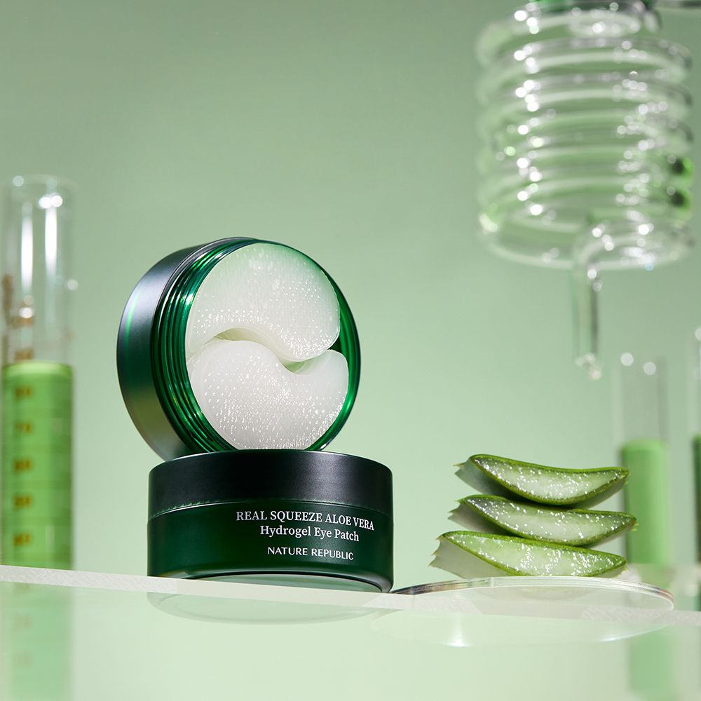 Barattolo verde con patch idrogel per occhi. Accanto, foglie di aloe vera. Vetreria da laboratorio sullo sfondo.