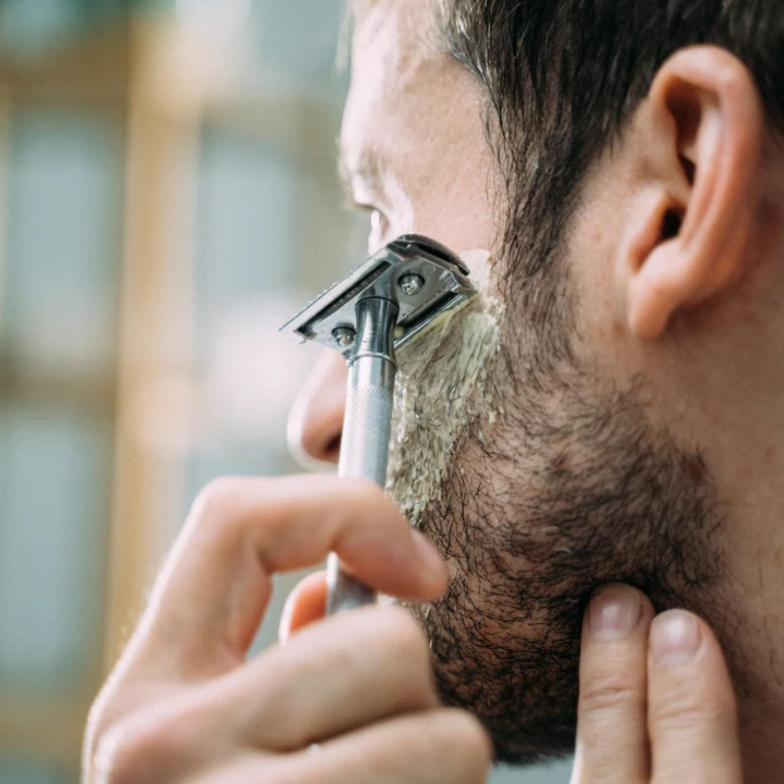 Uomo che si rade con il rasoio. Schiuma sulla barba. Primo piano.