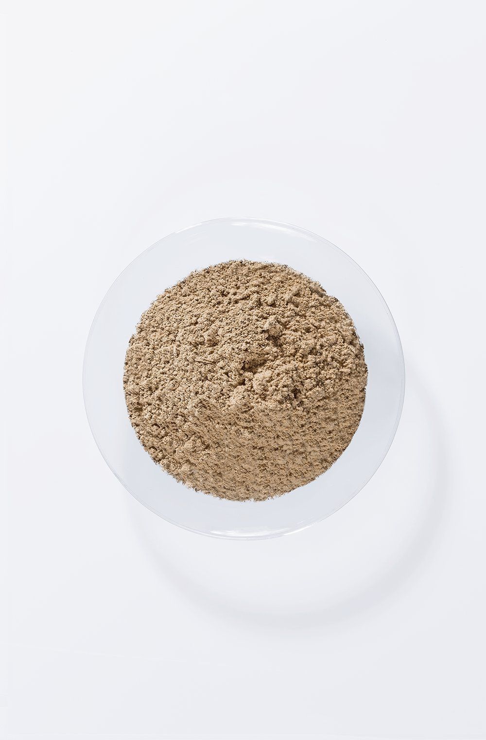 Polvere marrone in una ciotola di vetro trasparente. Vista dall'alto su sfondo bianco.