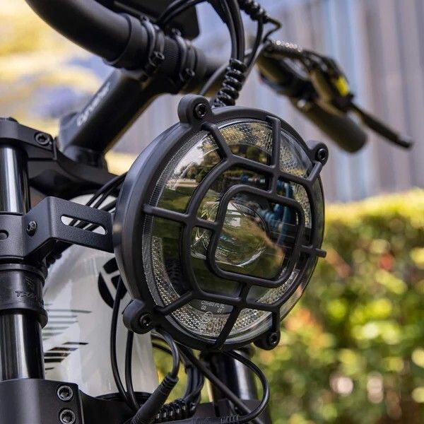 Faro bici rotondo con griglia protettiva. Alloggiamento nero, lente trasparente. Fissato sulla forcella.