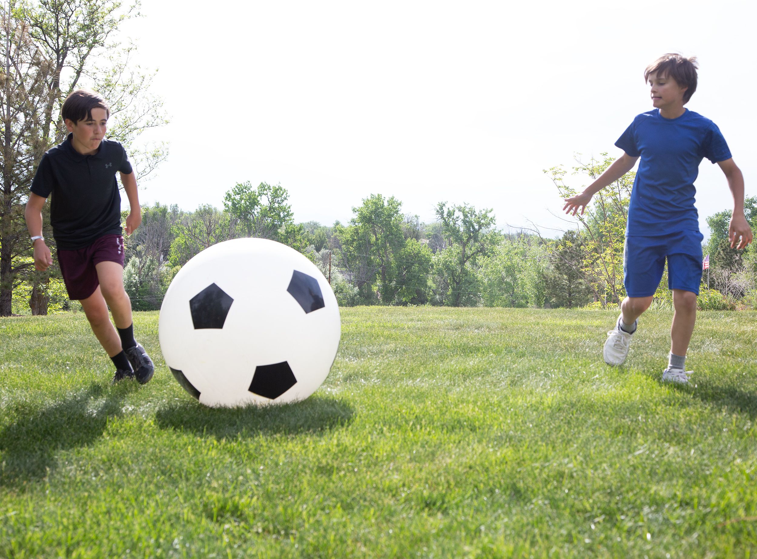 Due bambini giocano con un grande pallone da calcio bianco con pentagoni neri su un prato.