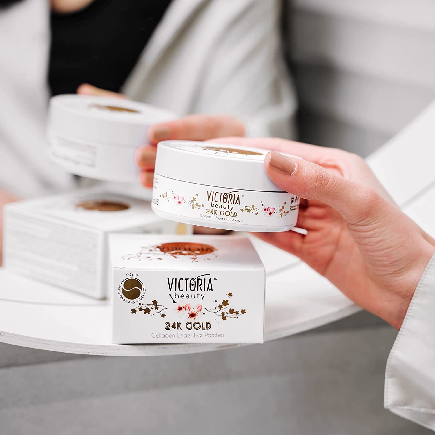Diverse confezioni del prodotto. Contenitori bianchi con logo e testo. Scritta: 24K Gold, Collagen Under Eye Patches.
