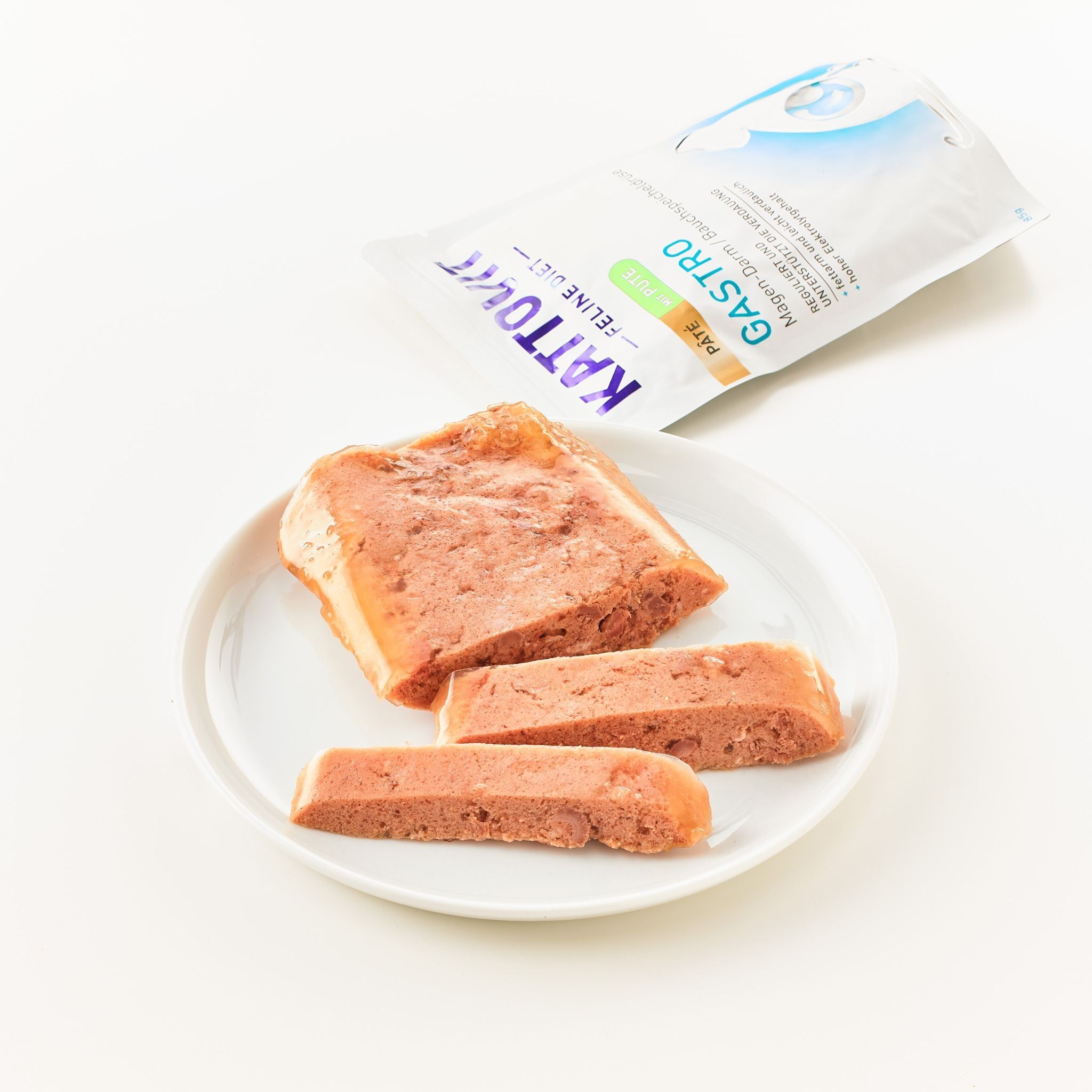 Piatto con tre pezzi di KATTOVIT Gastro Paté Huhn. Pezzi di paté rosa su piatto bianco. Confezione sullo sfondo.