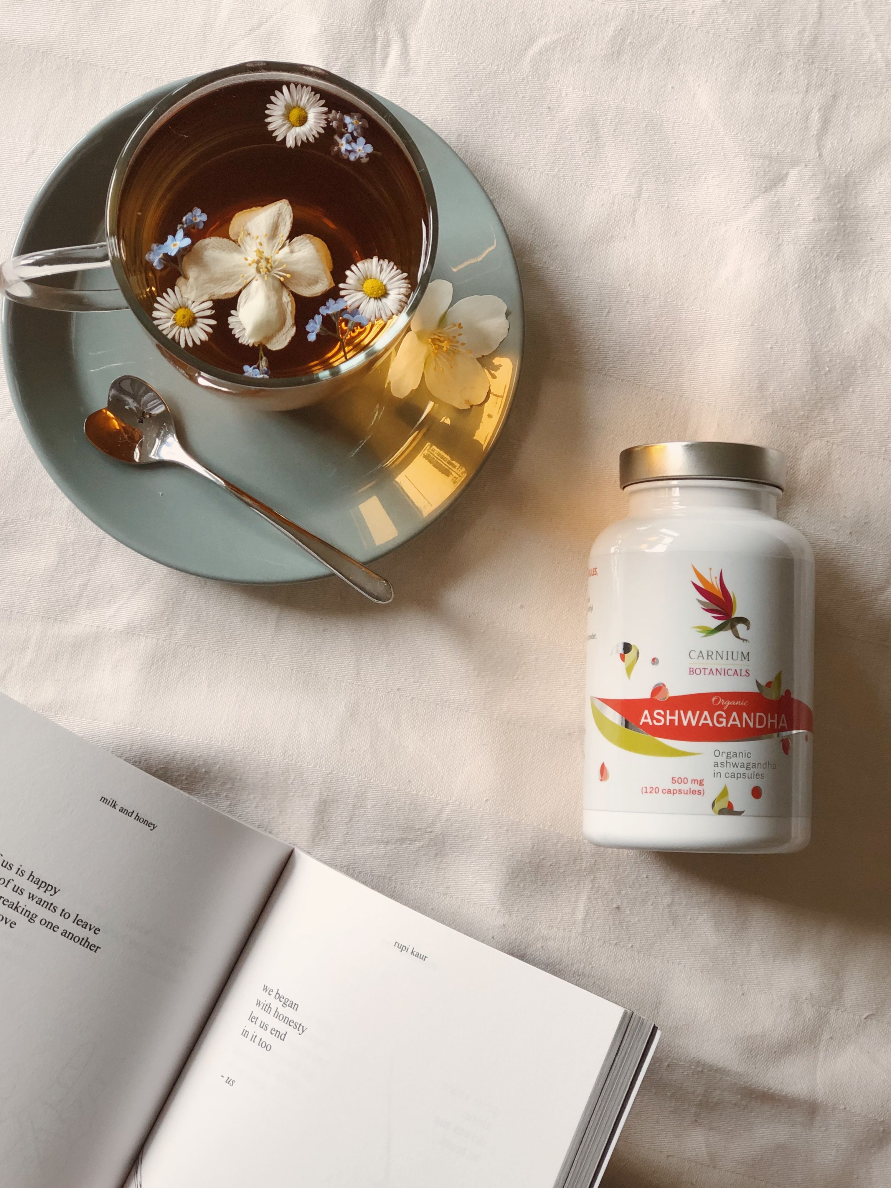 Flacone di capsule accanto a una tazza di tè e un libro aperto. Etichetta con nome del prodotto e logo.