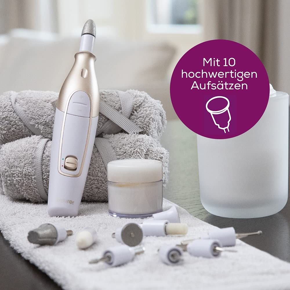 Dispositivo per la cura delle unghie bianco e oro con accessori. Testo: Con 10 attacchi di alta qualità. Su un asciugamano, accanto a crema e contenitore.