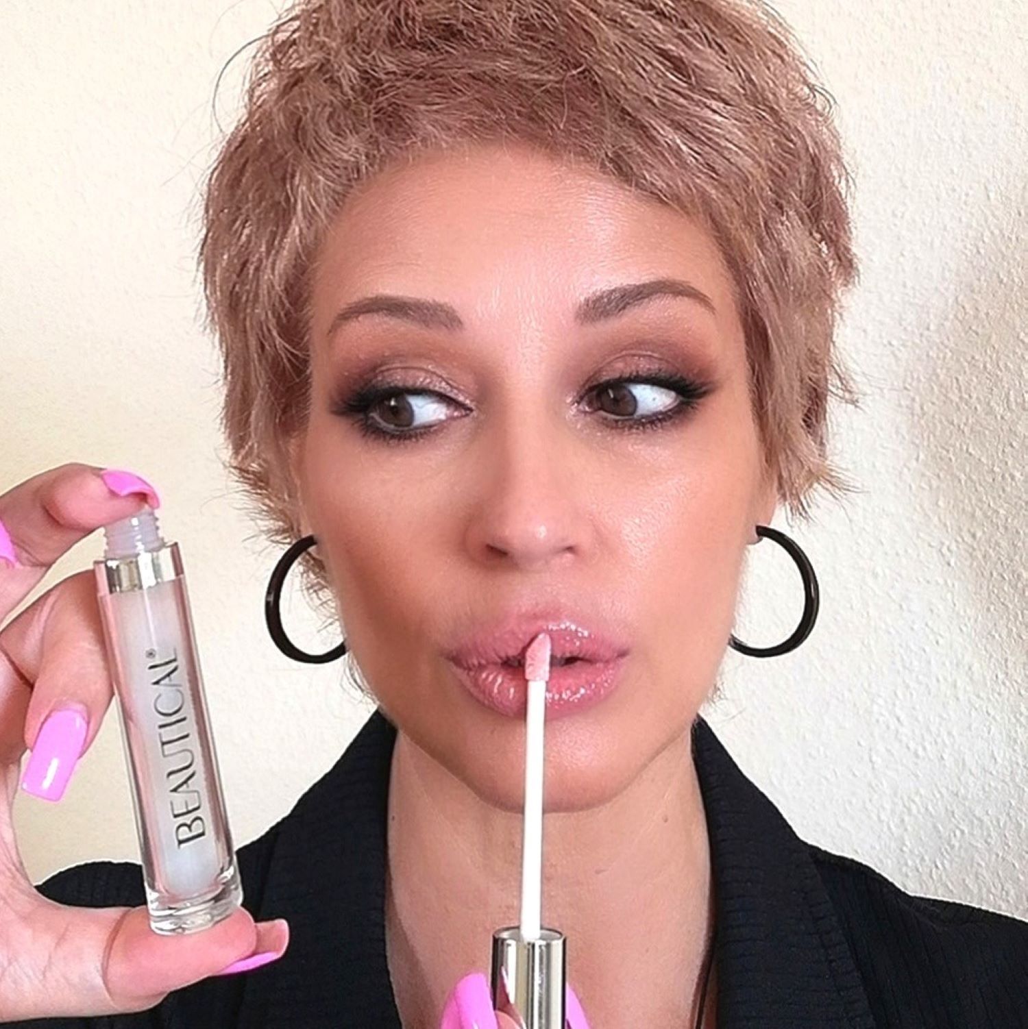 Donna tiene BEAUTICAL Instant Lip Plumper. Indossa rossetto e guarda di lato. Orecchini neri.