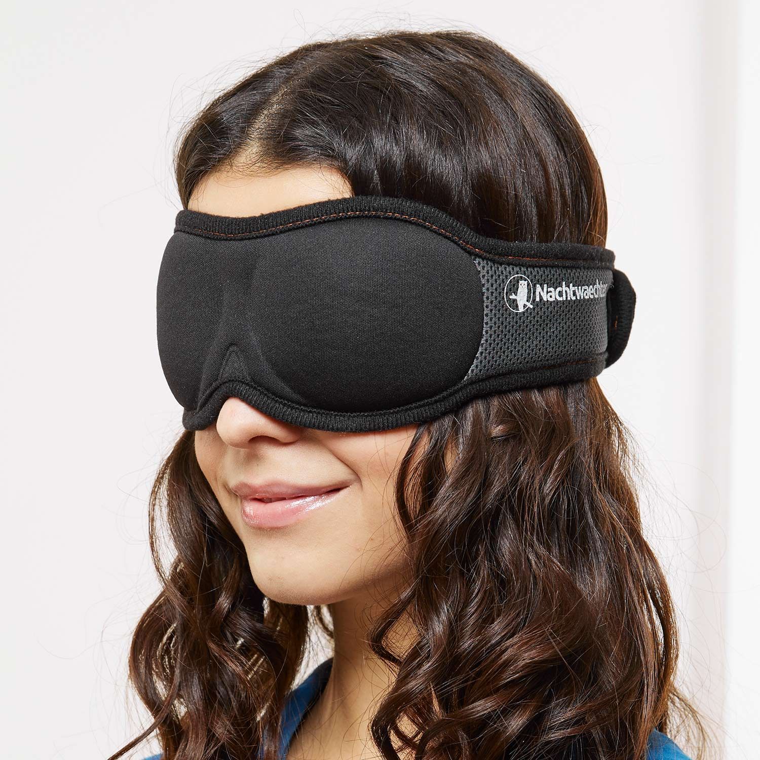 Donna con maschera per dormire nera. Fascia grigia con logo, maschera sugli occhi.
