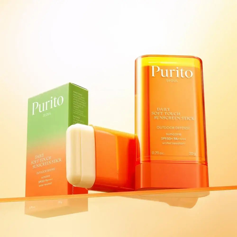 Stick arancione, scatola verde e stick. Testo: PURITO, Daily Soft Touch Sunscreen Stick.