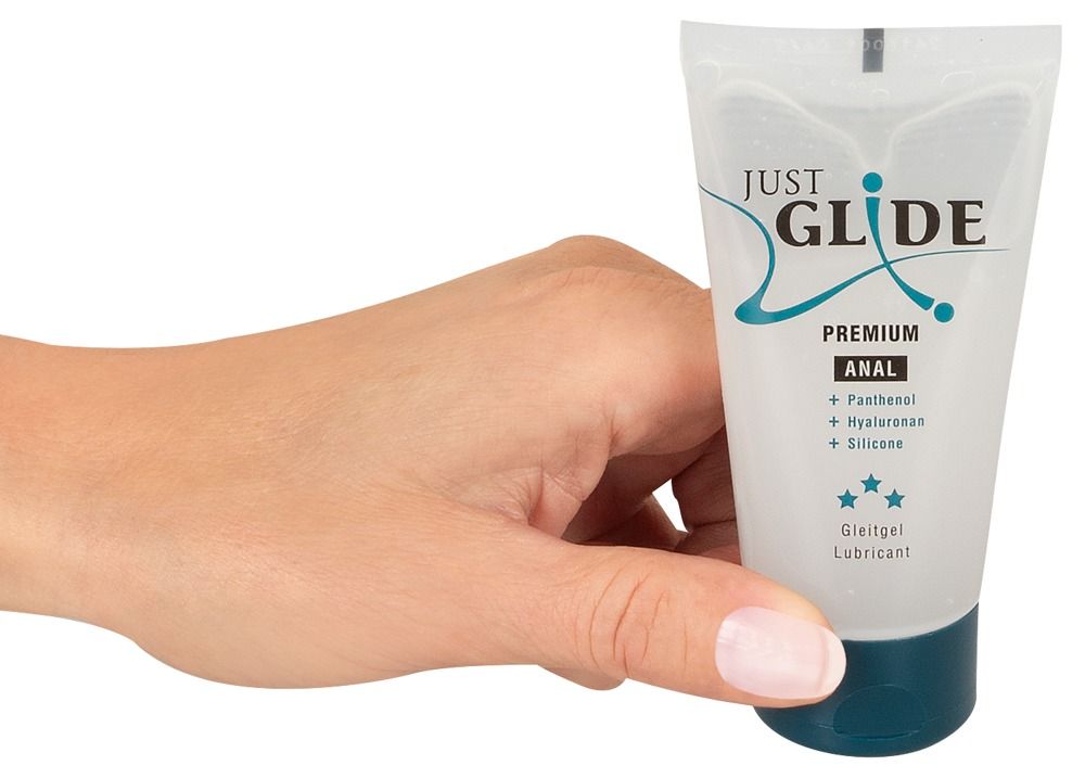 Mano che tiene un tubo. Scritta: Just Glide Premium Anal. Contiene Pantenolo, Ialuronano, Silicone. Gel lubrificante medico. Gel trasparente.