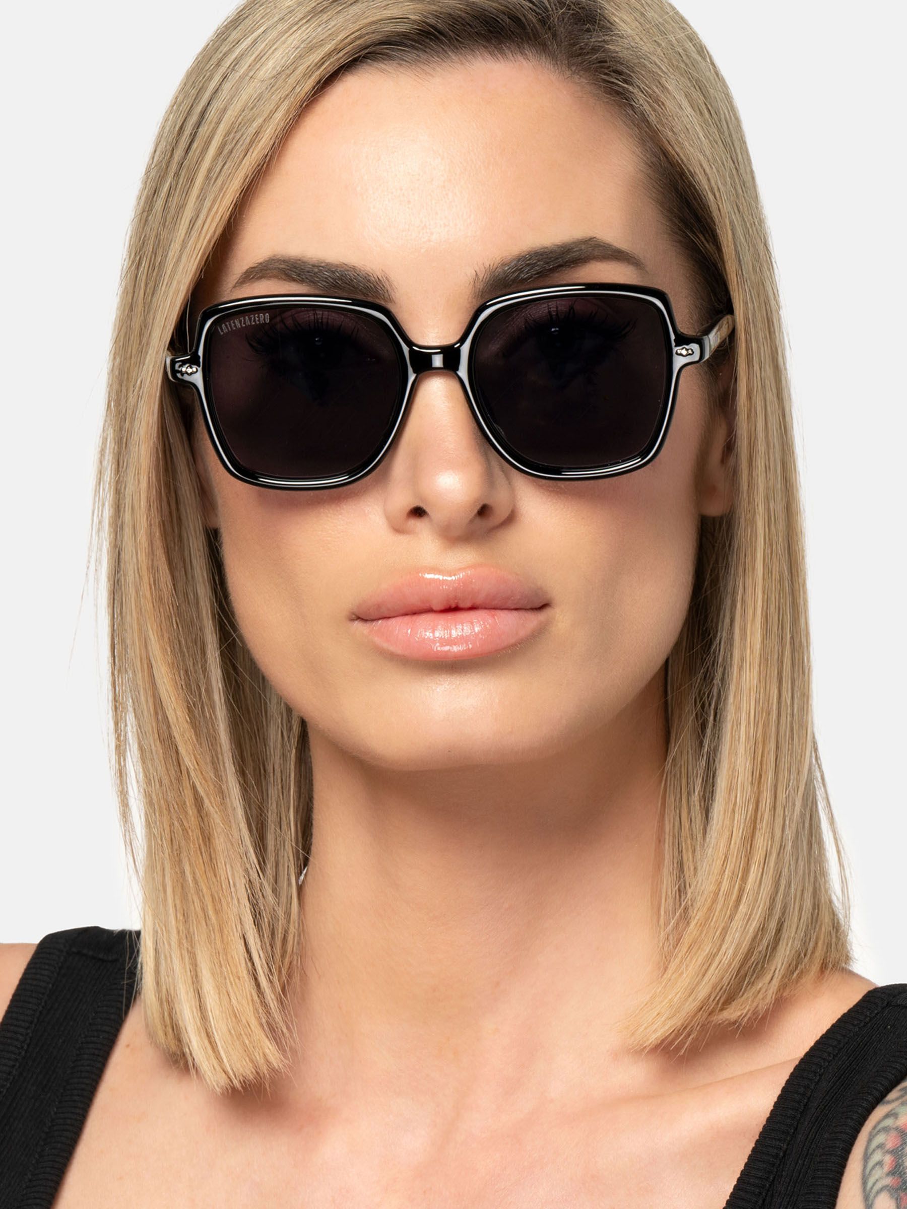 Donna con occhiali da sole neri. Lenti quadrate, montatura nera. Latenzazero sull'asta.