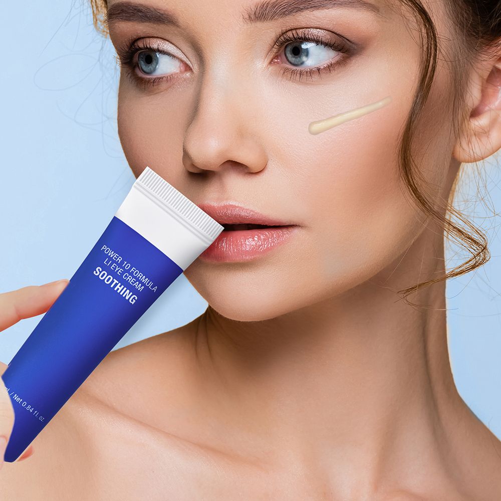 Donna tiene tubo blu. Scritta: POWER 10 FORMULA LI EYE CREAM SOOTHING. Crema sulla pelle.