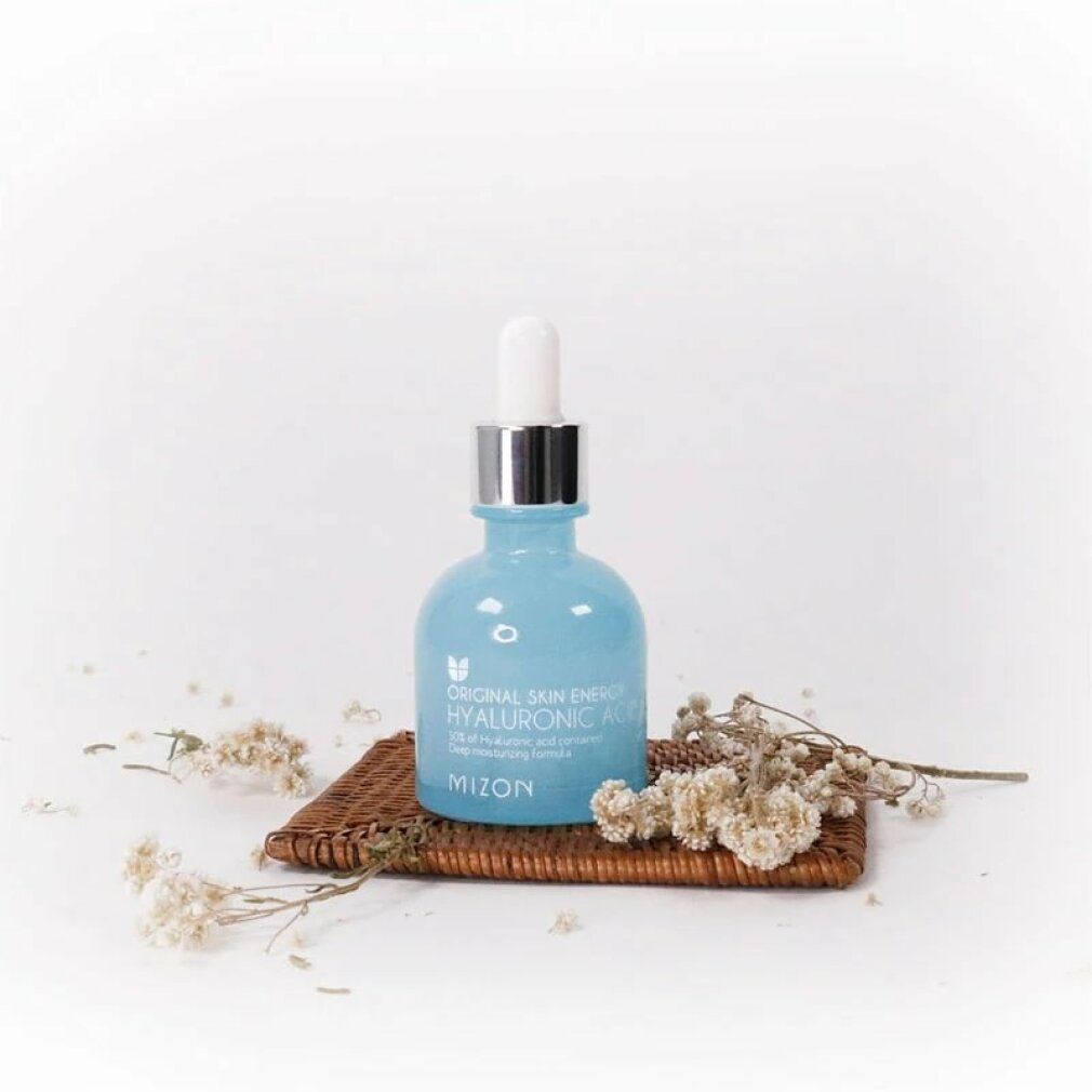 Flacone azzurro con tappo argentato e contagocce su un piccolo vassoio con fiori secchi. Marchio: Mizon.