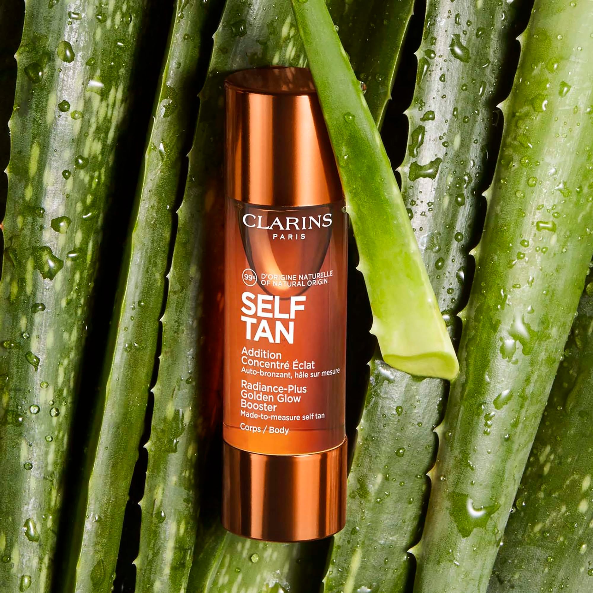 Flacone marrone con tappo dorato su foglie di aloe vera. Testo: Clarins, Self Tan.