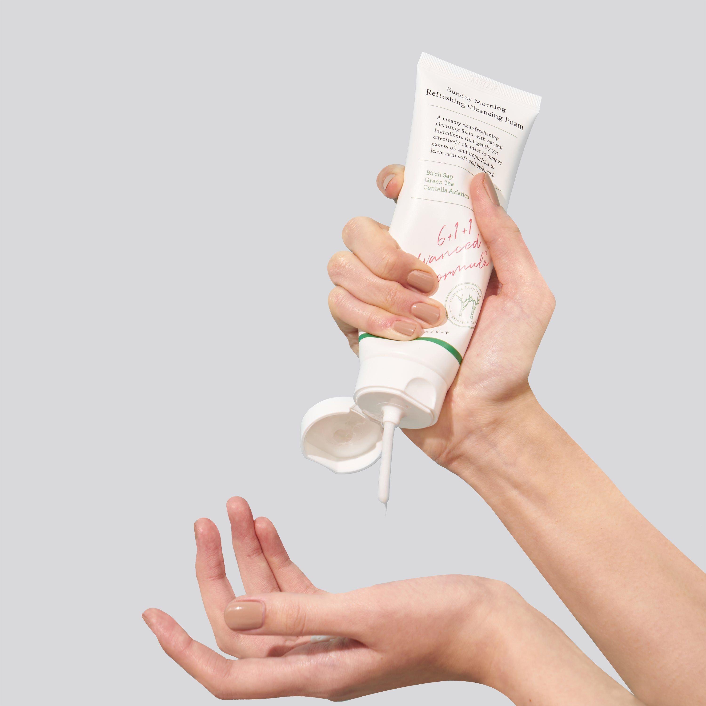 Mani che tengono un tubo. La crema esce dall'apertura. Scritto: Sunday Morning Refreshing Cleansing Foam.