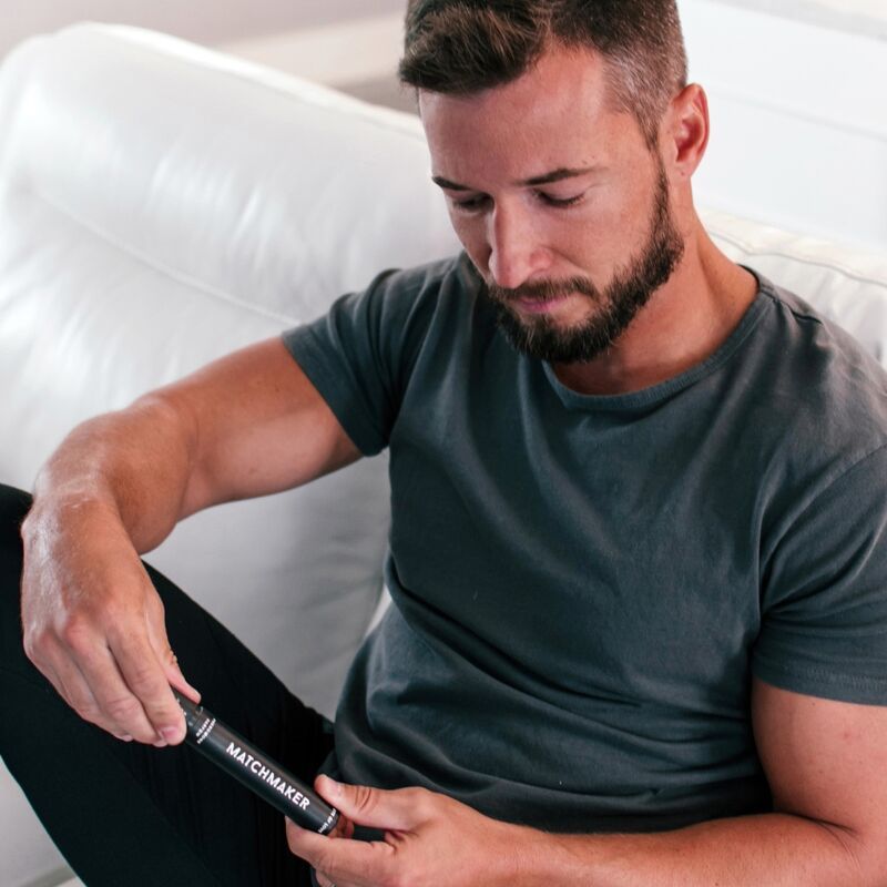 Uomo che tiene la confezione del profumo. Confezione cilindrica nera con scritta bianca MATCHMAKER.
