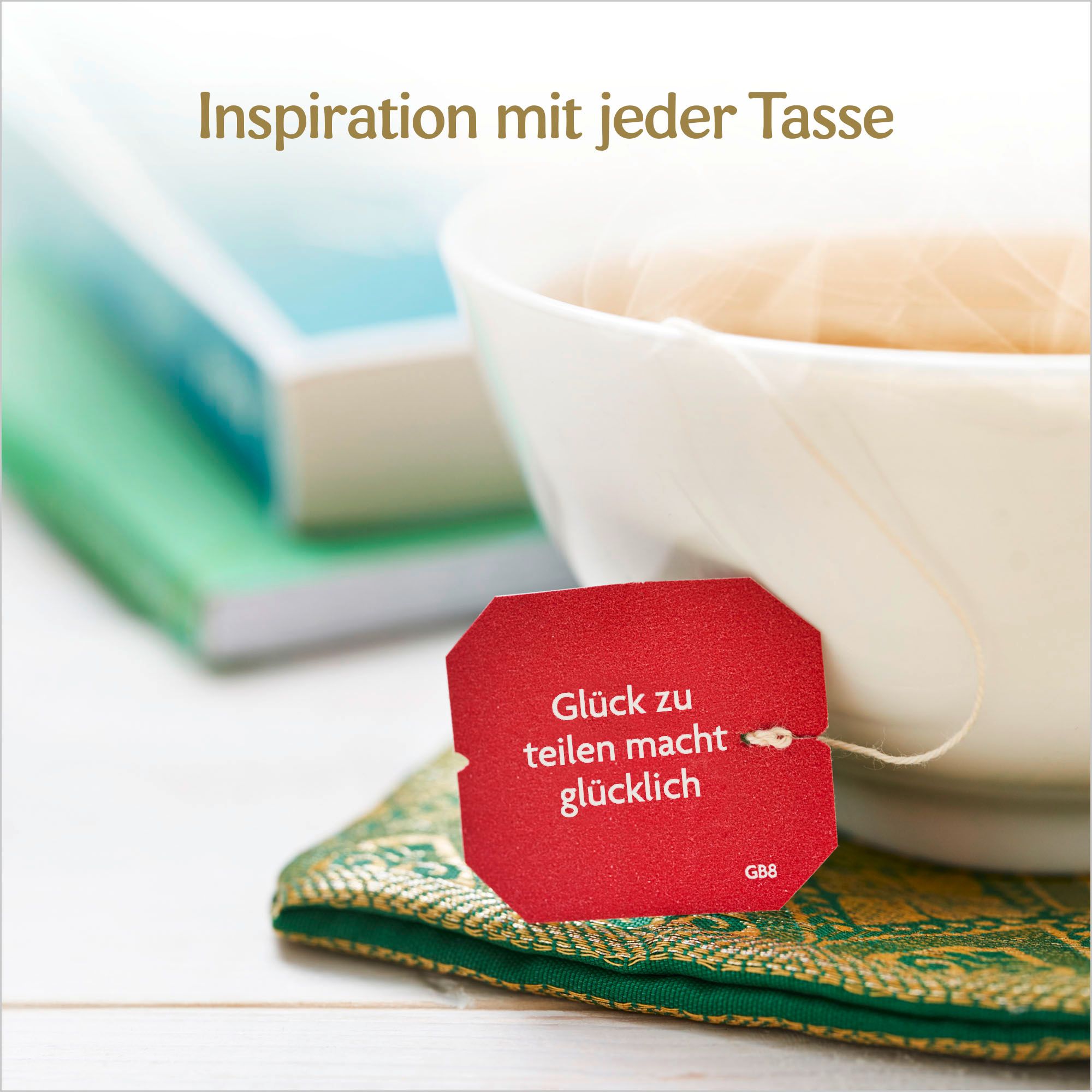 Tazza con bustina di tè. Etichetta rossa con testo. Su sottobicchiere verde. Libri sullo sfondo.