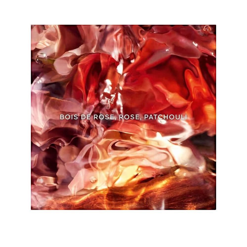 Confezione quadrata con design floreale. Testo: Bois de Rose, Rose, Patchouli. Sfumatura di colori rossi e arancioni.