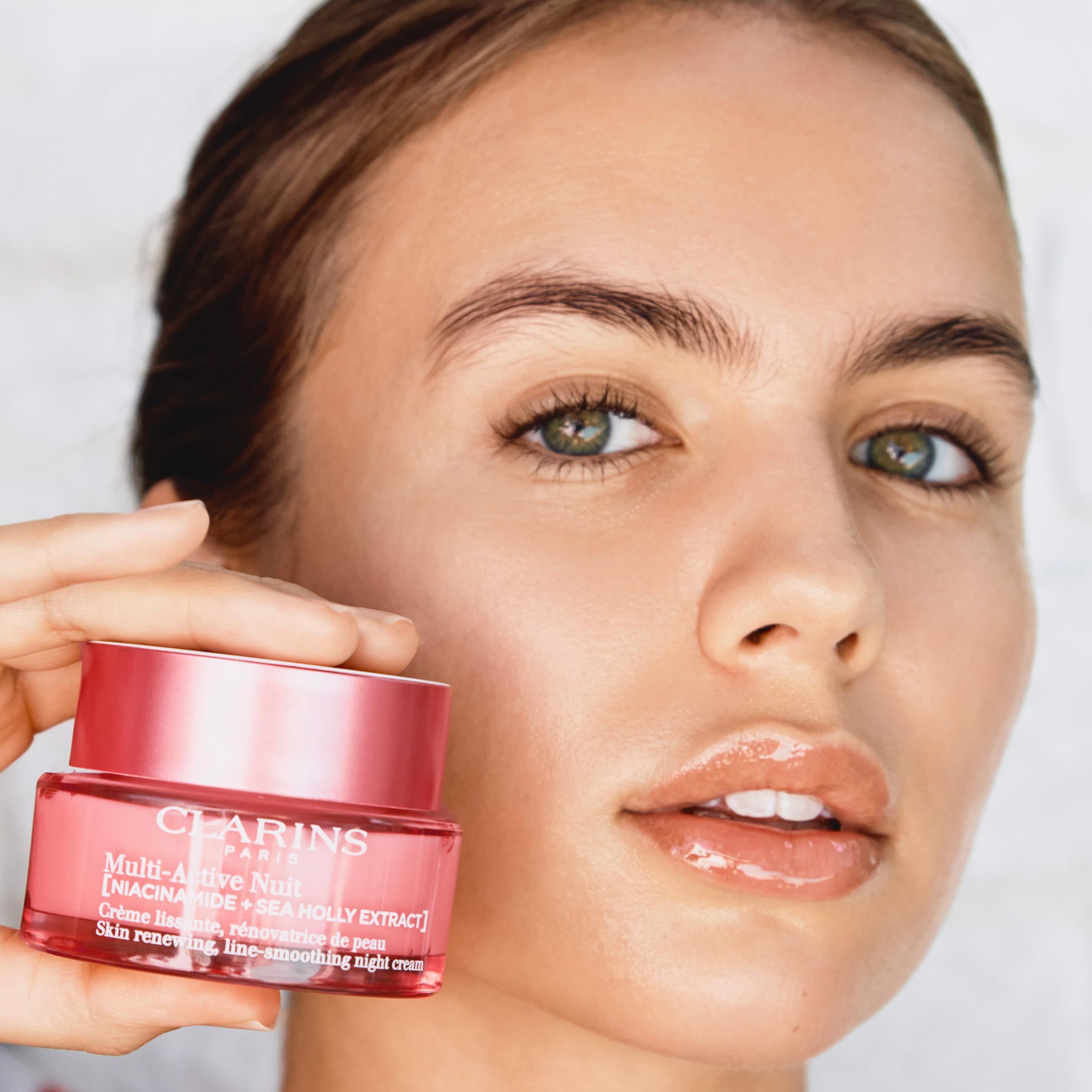 Donna che tiene un vasetto di crema rosa. Scritta: CLARINS PARIS, Multi-Active Nuit. Testo: Skin renewing, line-smoothing night cream.