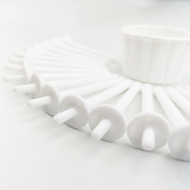 Molti applicatori bianchi per cera nasale sono disposti a cerchio attorno a una piccola tazza bianca.