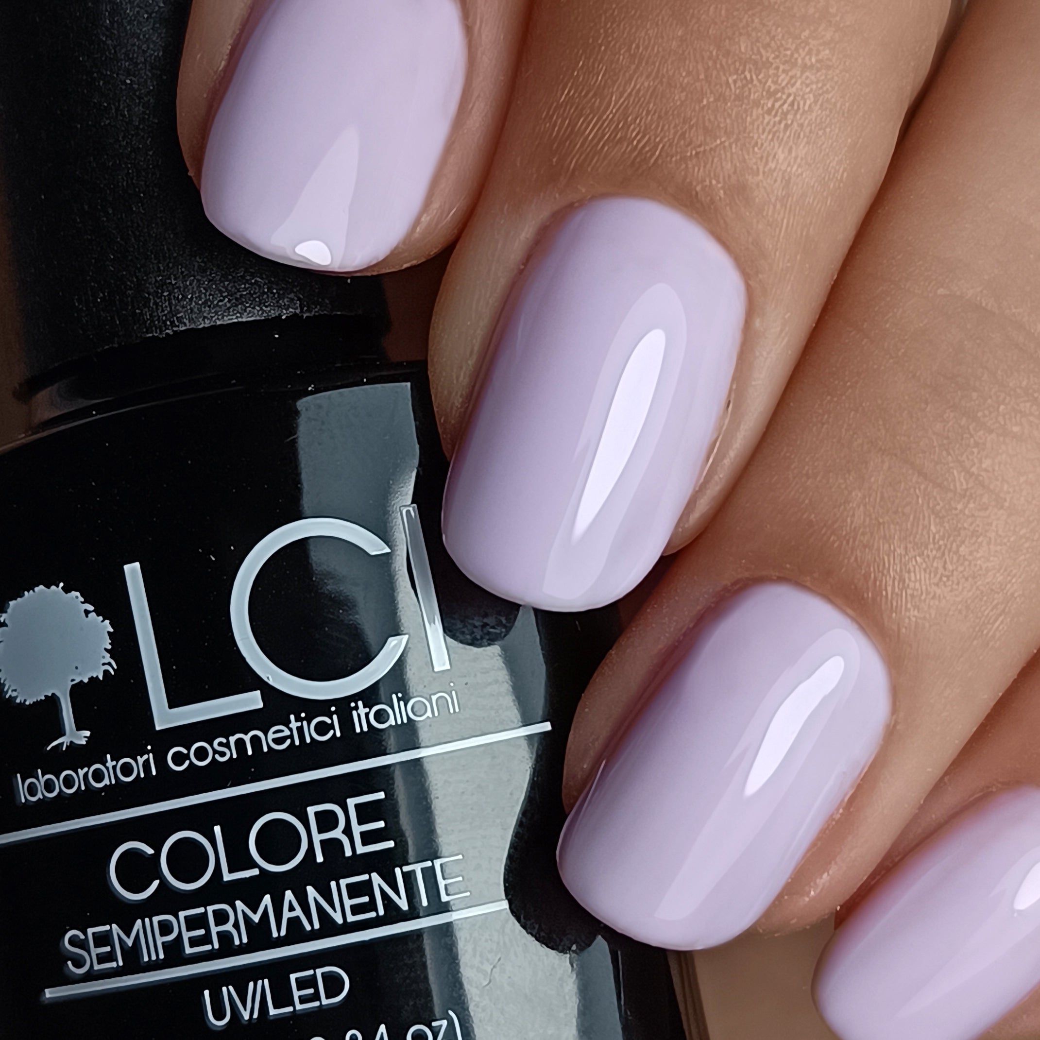 Mano con unghie lilla smaltate. Flacone con scritta: LCI, Colore Semipermanente, UV/LED.