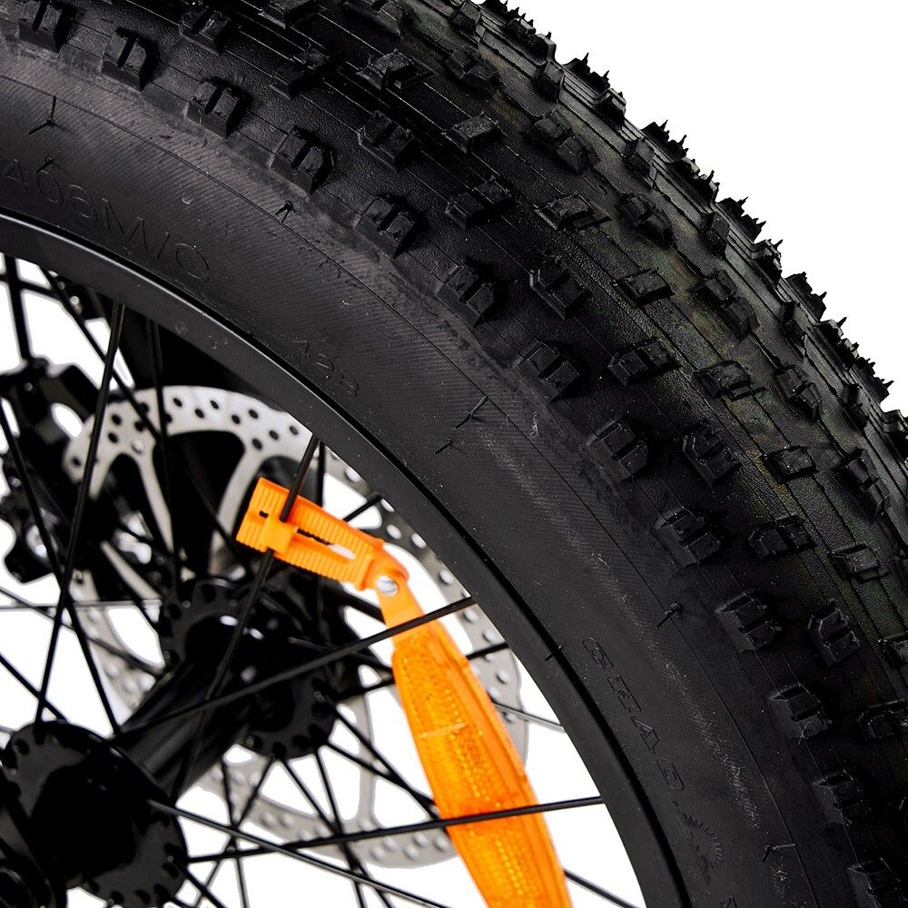 Primo piano di uno pneumatico nero per bicicletta con battistrada ruvido. Freni a disco e ruota a raggi visibili. Riflettore arancione.