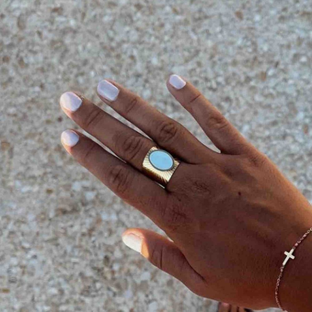 Mano con unghie smaltate di grigio chiaro. Anello dorato con pietra blu. Braccialetto con croce.
