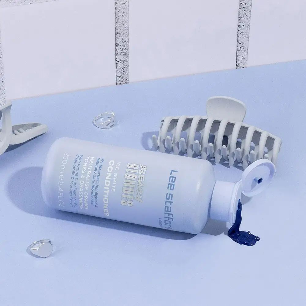 Flacone azzurro chiaro sdraiato. Fermagli per capelli e accessori trasparenti. Prodotto: LEE STAFFORD Bleach Blondes Conditioner.
