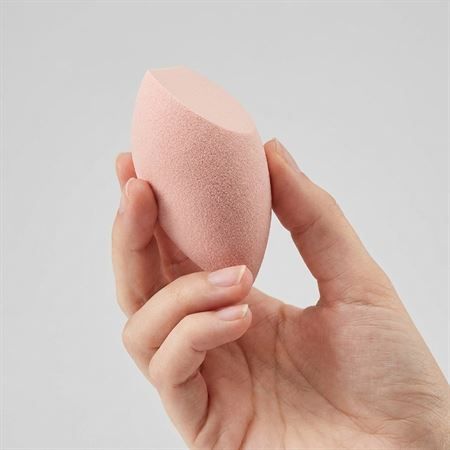Una mano tiene una spugnetta per il trucco rosa con punta smussata.