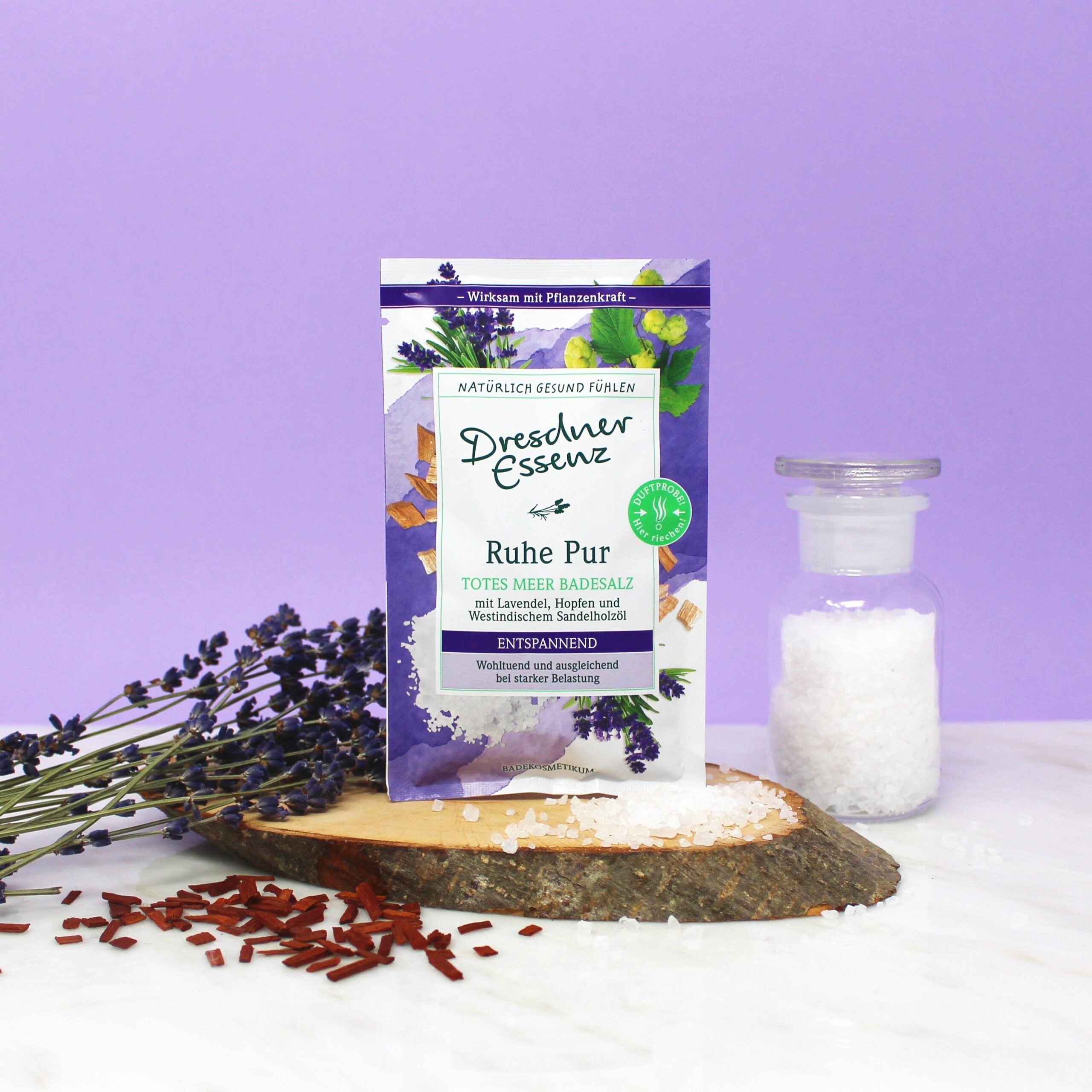 Bustina di sali da bagno Dresdner Essenz Ruhe Pur su ceppo di legno, accanto a lavanda e barattolo di vetro.